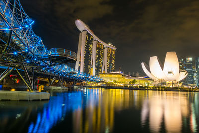 Marina bay sands by bay of water against sky in illuminated city at night