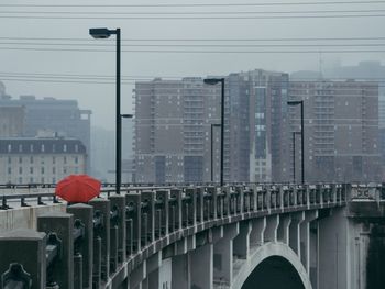 Person walking with red umbrella on bridge against cloudy sky