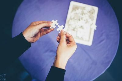 Cropped hands of woman holding jigsaw puzzles over table