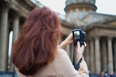 Rear view of woman photographing building with camera in city