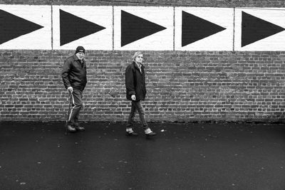 Full length of people walking on street against brick wall