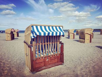 Hooded chairs at sandy beach against sky