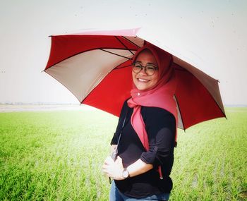 Portrait of smiling woman holding umbrella while standing on field