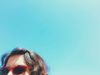 Low angle view of woman wearing sunglasses against clear blue sky