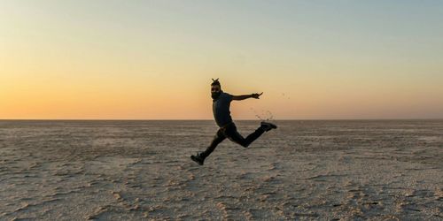 Man in mid-air jumping at white desert in kutch against clear sky during sunset