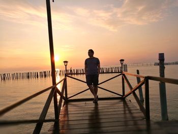Man standing on pier over sea against sky during sunset