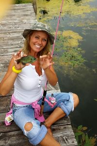 Portrait of smiling mid adult woman showing fish on pier over lake