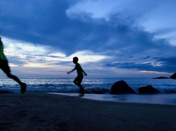 Silhouette men on beach against sky during sunset
