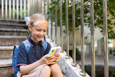 Portrait of happy boy holding mobile phone while sitting on railing