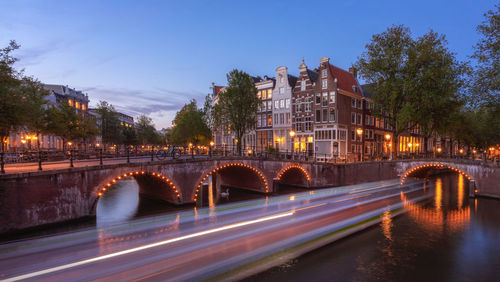 Light trails on bridge over canal against sky in city