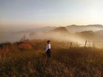 Woman standing on field against sky during foggy weather