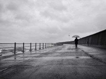 Full length of person with umbrella walking on footpath by sea against sky