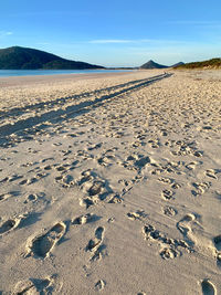 Footprints on sand at beach against blue sky