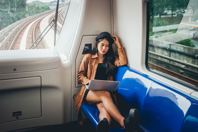 Full length of woman using laptop while sitting in train