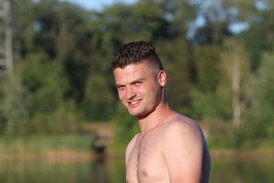 Portrait of shirtless man standing against trees in forest