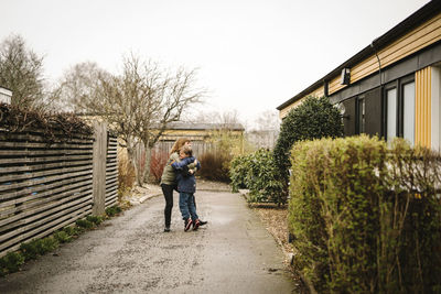 Mother embracing son with down syndrome while standing on street by house