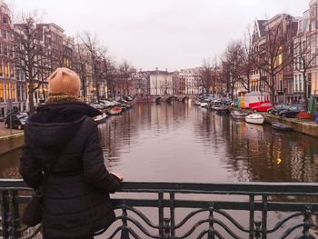 Rear view of man on bridge over canal in city