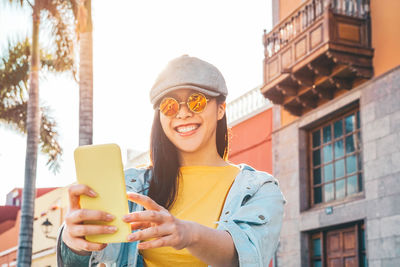 Smiling young woman taking selfie in city during sunny day