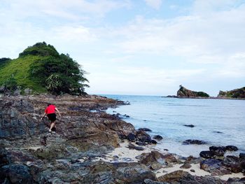 Rear view of person on rock by sea against sky