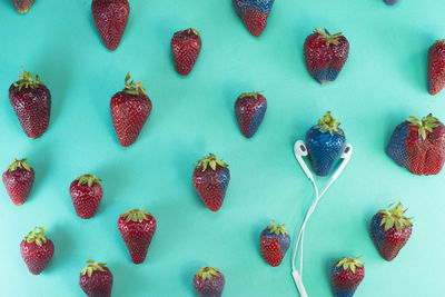 High angle view of strawberries and headphones against turquoise background