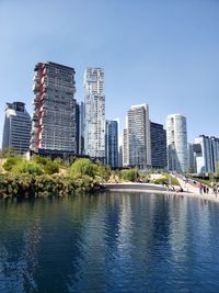 Modern buildings by river against clear sky