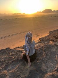 Rear view of woman sitting on rock at desert during sunset