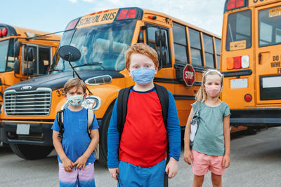 Three children kids students in protective face masks near school yellow bus outdoors. new normal 