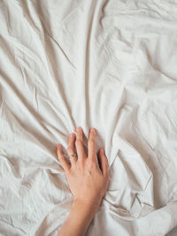 Woman's hand on crumpled bed sheet. creased white linen. cozy imperfect house. non-ideal cozy home.