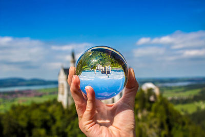 Close-up of hand holding crystal ball against blue sea