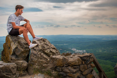 Full length of man sitting on rock against sky
