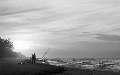 Silhouette people fishing on beach against sky