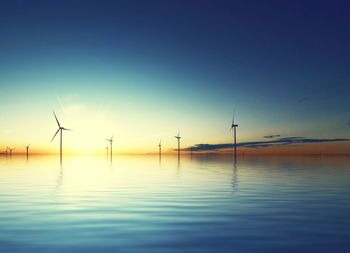 Traditional windmill by lake against sky during sunset