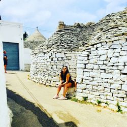 Full length portrait of woman sitting against building