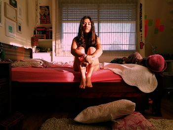 Young woman sitting on bed at home