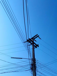 Low angle view of silhouette electricity pylon against blue sky