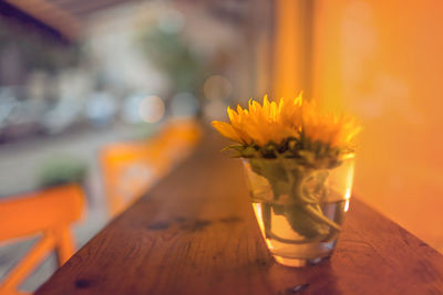 Close-up of yellow flowers in glass on wooden table