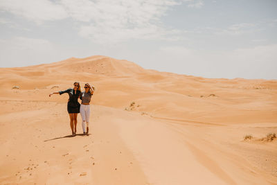 Smiling young friends walking at desert against sky