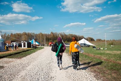 Rear view of people walking on field against sky