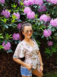 Portrait of beautiful woman standing by pink flowering plants