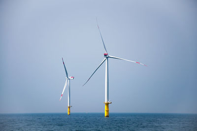 Wind turbines in sea against clear sky