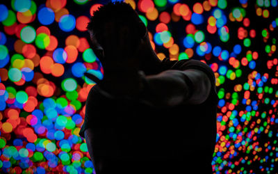 Rear view of man standing against illuminated multi colored lights