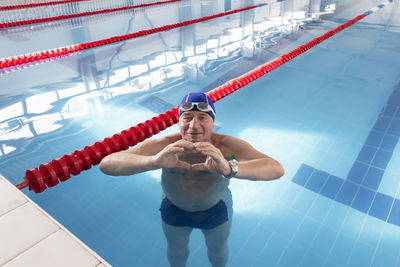 An elderly man stands in a pool of water and shows a heart with his hands goes in for sports,  relax