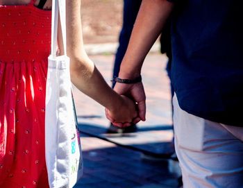 Midsection of couple holding hands while standing on street