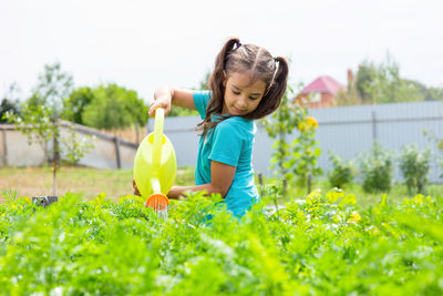 Smiling little girl in a green t-shirt, watering a green bed of yellow watering can, in the garden