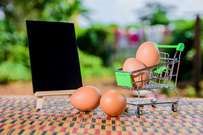 Close-up of brown eggs with shopping cart and blank signboard on table at yard