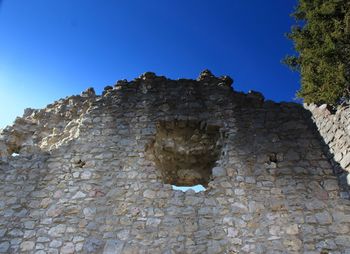 Low angle view of stone wall against clear blue sky