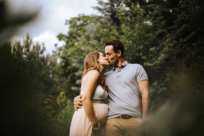 Low angle view of couple kissing while standing against trees in forest