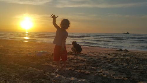 Children playing at beach against sky during sunset