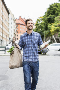 Full length portrait of happy man with groceries walking on street