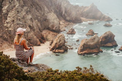 Rear view woman sitting on rock by sea against sky